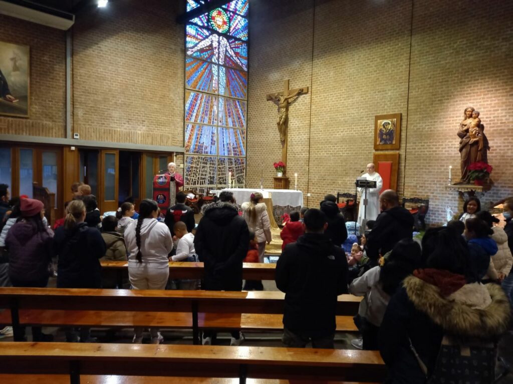 Fieles escuchando al cura, delante de un gran crucifijo con nuestro Señor Jesús crucificado.